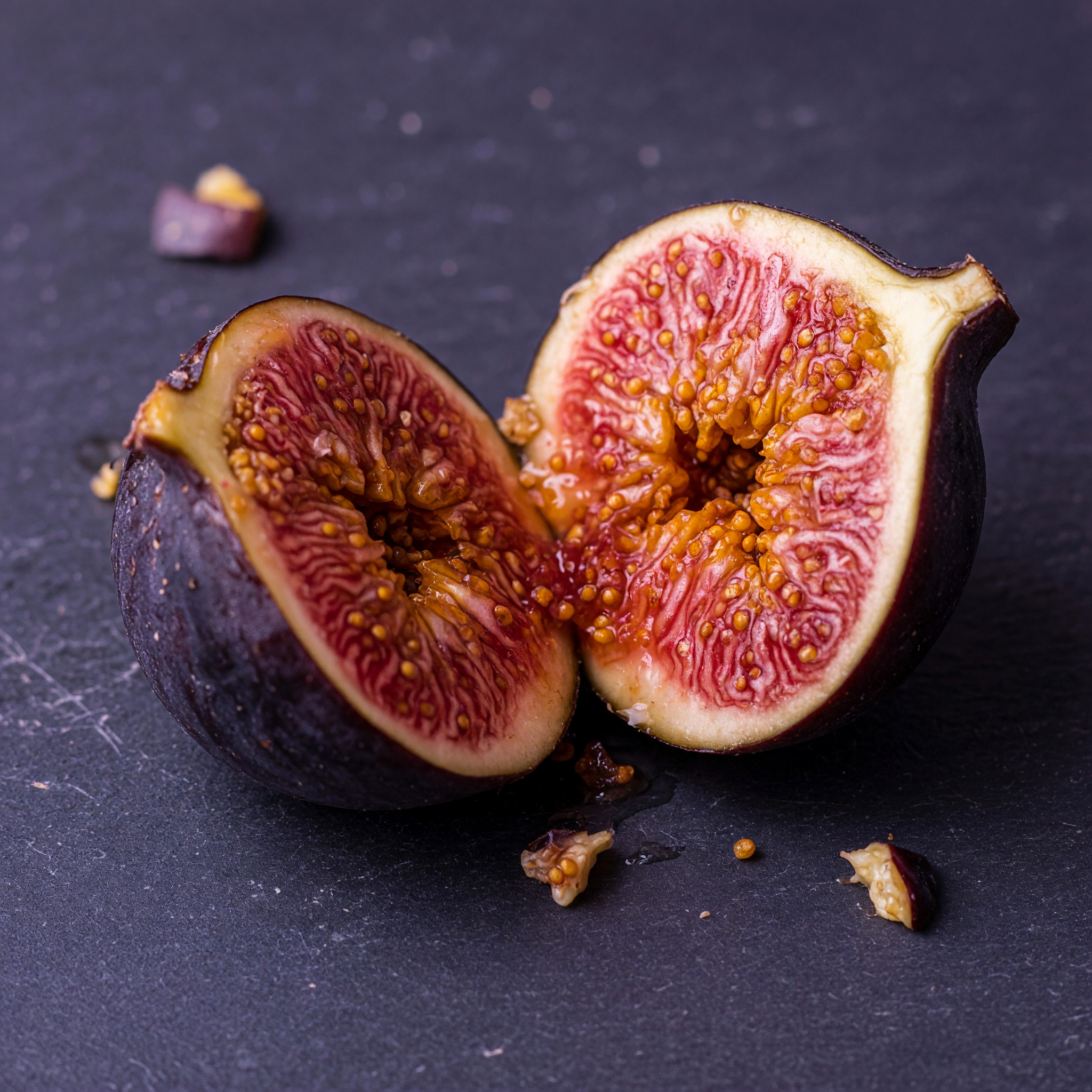 A single ripe fig split open on dark slate, macro food photography